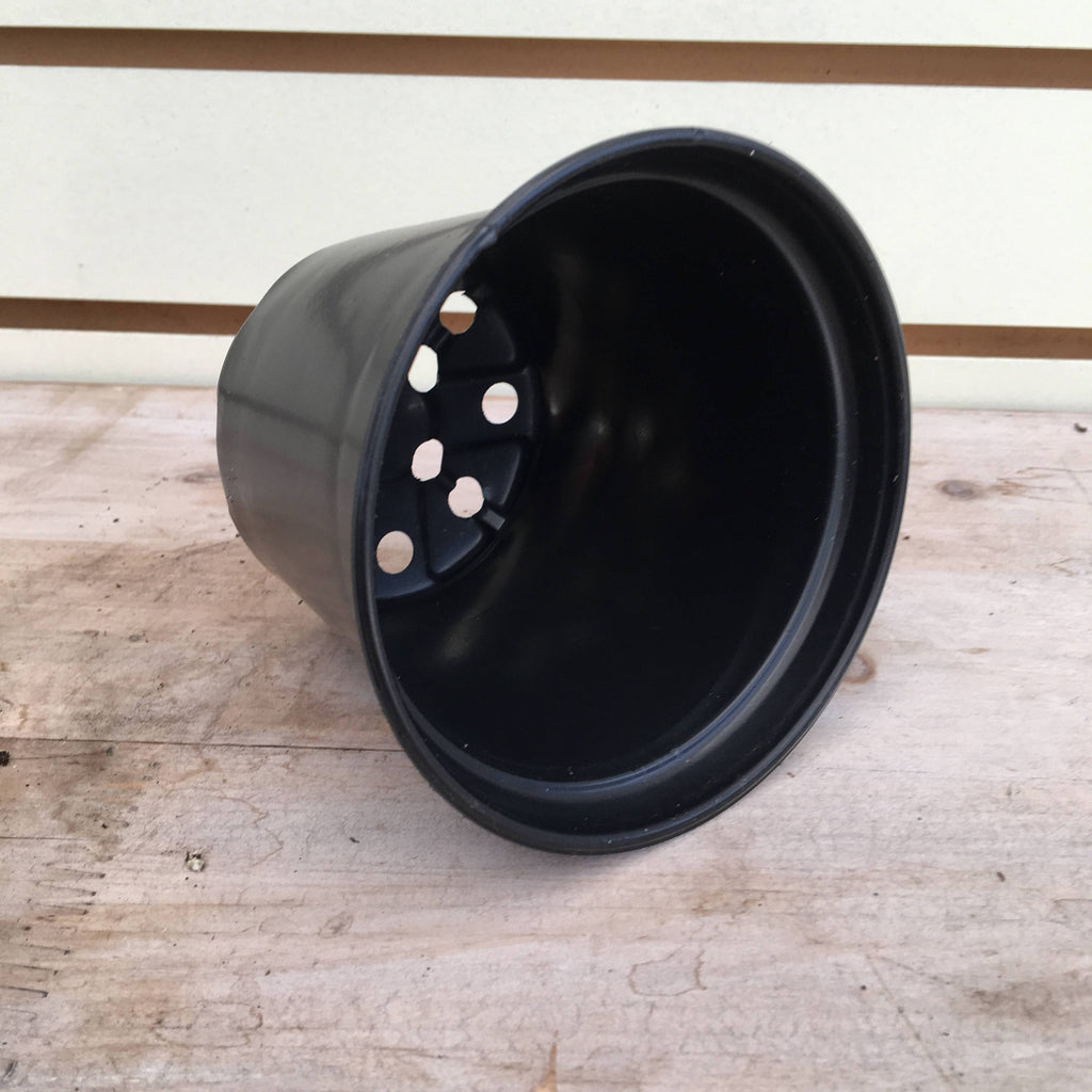 Black 4-inch plastic growing pot lying on its side with drainage holes